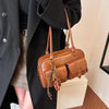 Eine braune Handtasche mit mehreren Taschen wird von einer Person in einem schwarzen Mantel getragen.