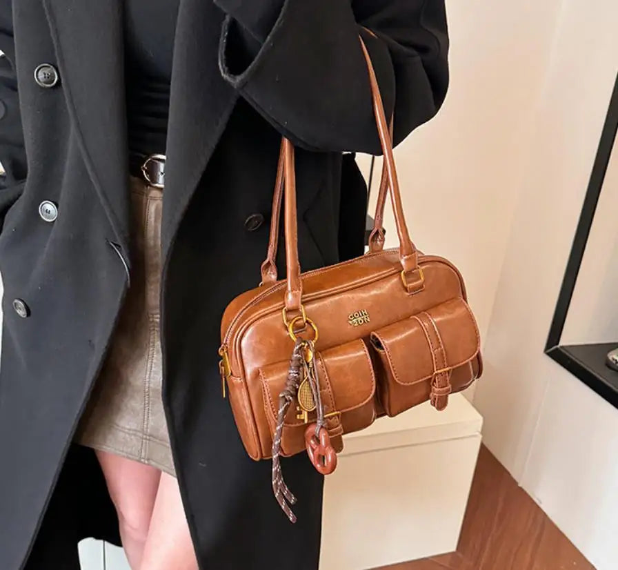 Eine braune Handtasche mit mehreren Taschen wird von einer Person in einem schwarzen Mantel getragen.