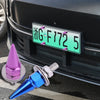 A close-up of a green license plate with characters and numbers mounted on a black car grille, next to a silver screw kit.