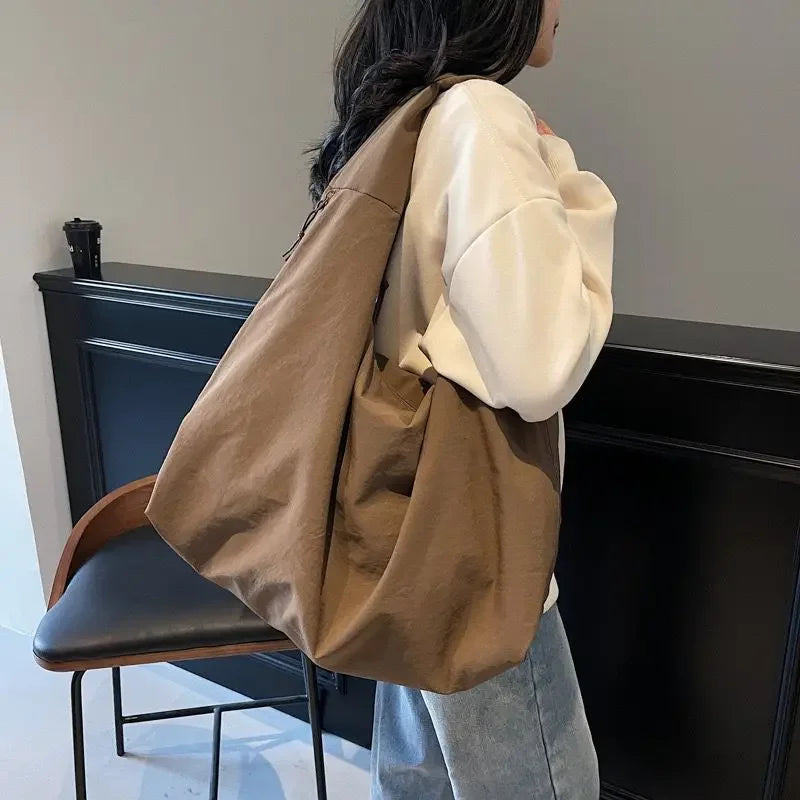 A person is holding a brown lightweight nylon tote bag with a secure zipper closure against a dark cabinet.