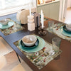 A dark wooden table set featuring four vintage chicken and daisy patterned placemats, ceramic bowls, and silverware.