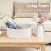 A white handwoven rope storage basket filled with magazines sits on a wooden table next to a pink floral arrangement.