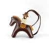A brown leather pony charm with a gold-toned buckle and checkered tag hanging from a leather strap.