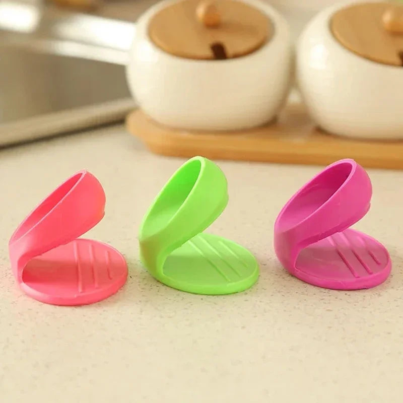 Three silicone finger covers in pink and green colors resting on a light surface near white ceramic dishes.