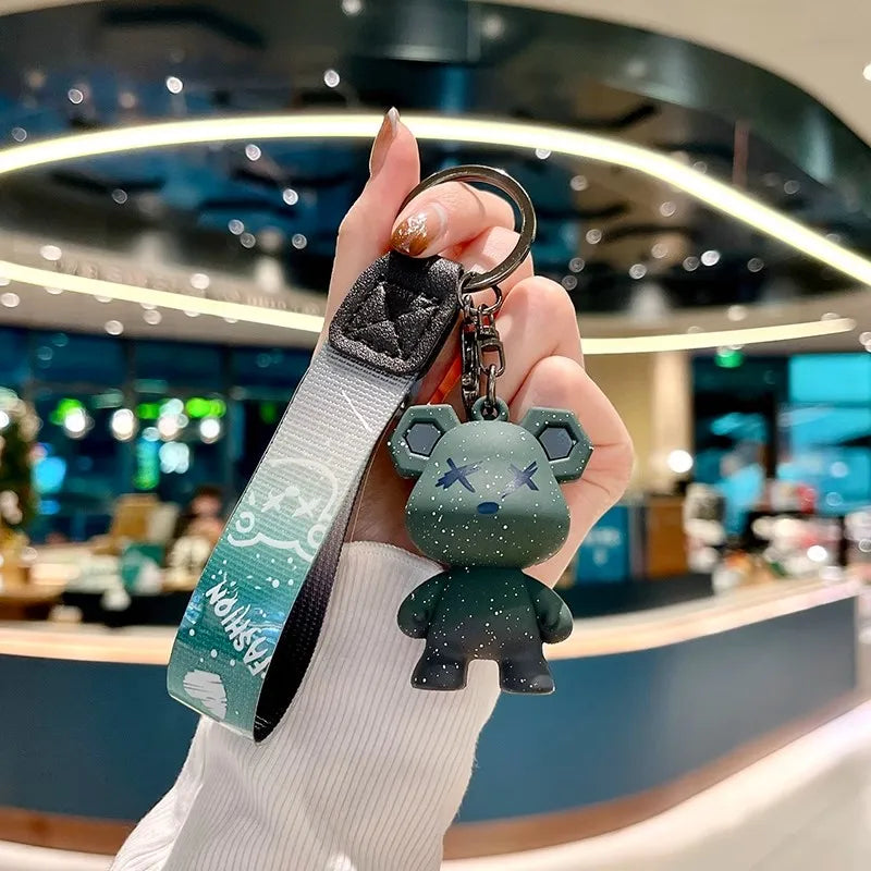 A hand holds a luxury leather key case featuring a cute green elephant charm against a blurred background.