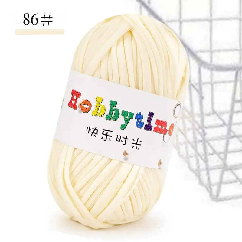 A ball of white soft T-shirt yarn for crochet and knitting is shown next to a wire basket.