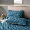 A teal quilted pillow protector resting on a bed, next to a headboard and a small vase.