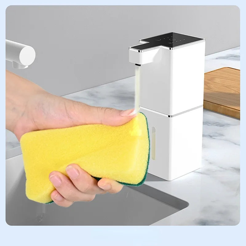 A hand is using a yellow sponge to clean a white touchless infrared smart soap dispenser.