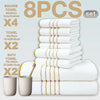 A set of eight white bath towels with gold stripes stacked and displayed next to a wooden brush.