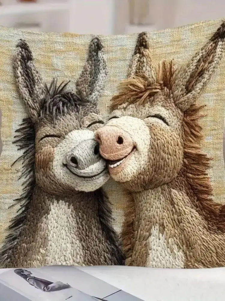 A knitted picture of two adorable donkeys with their faces touching on a beige cushion cover.