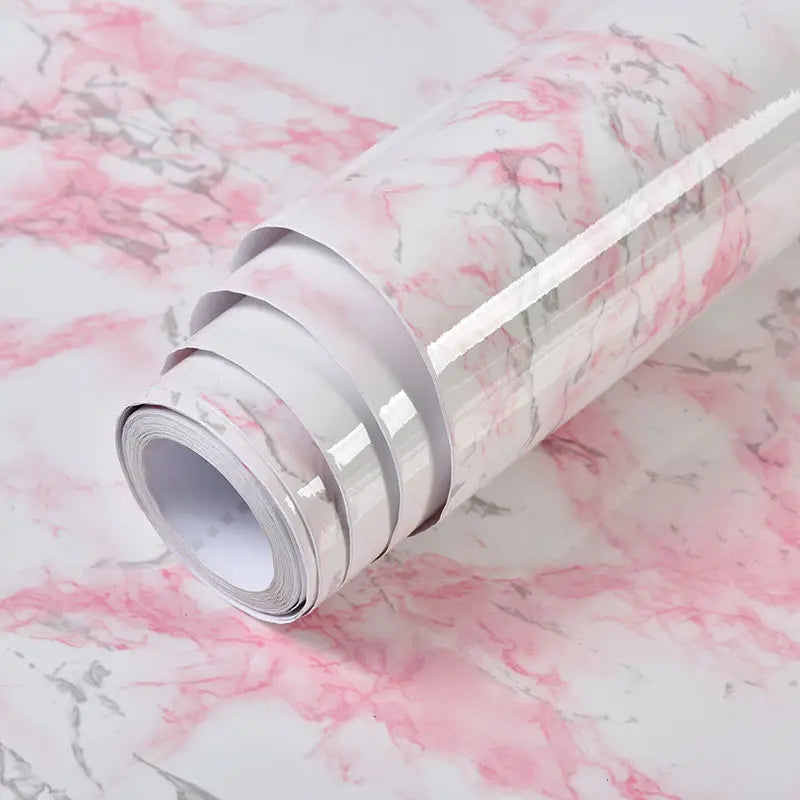 Roll of white marble contact paper with pink veining lying on a pink and white marble surface