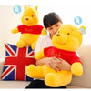 A woman is holding a large yellow Winnie the Pooh plush toy, which is red-shirted, in a domestic setting.