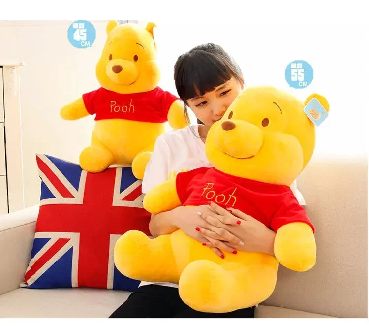 A woman is holding a large yellow Winnie the Pooh plush toy, which is red-shirted, in a domestic setting.