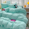 A light aqua bedding set featuring a duvet cover, flat sheet, and pillowcases with a small animal plush toy.