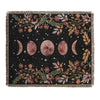 A dark fabric throw blanket featuring a bohemian floral and celestial pattern with moon shapes and foliage.