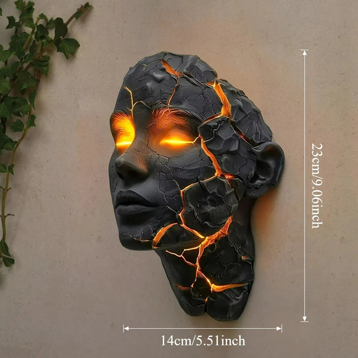 A dark, cracked face sculpture illuminated with orange light, mounted on a light-colored wall.