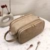 A tan waterproof PU leather cosmetic bag is shown resting on a white surface next to a ceramic vessel and makeup brushes.