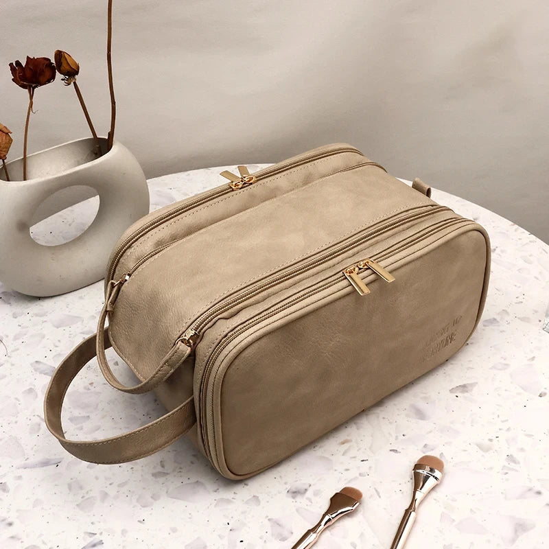 A tan waterproof PU leather cosmetic bag is shown resting on a white surface next to a ceramic vessel and makeup brushes.