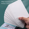 A stack of white 300g thickened paper sheets is shown being held, with a tin box visible below.