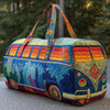 A colorful quilted travel duffle bag with patterned fabric and striped straps resting on a gray surface.