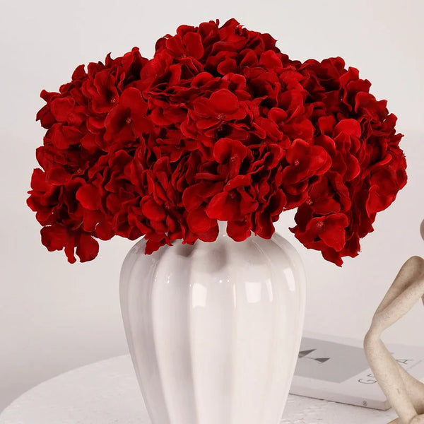 A bouquet of vibrant red silk hydrangea flowers displayed in a white vase.