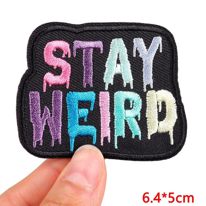 A set of embroidered iron-on letter patches in various colors including pink purple and teal on a black fabric
