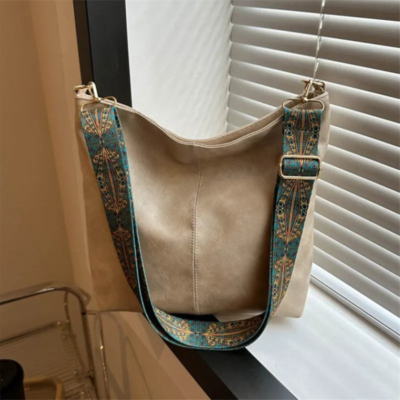 A tan vintage bohemian shoulder bag with golden embroidery hanging by a window.