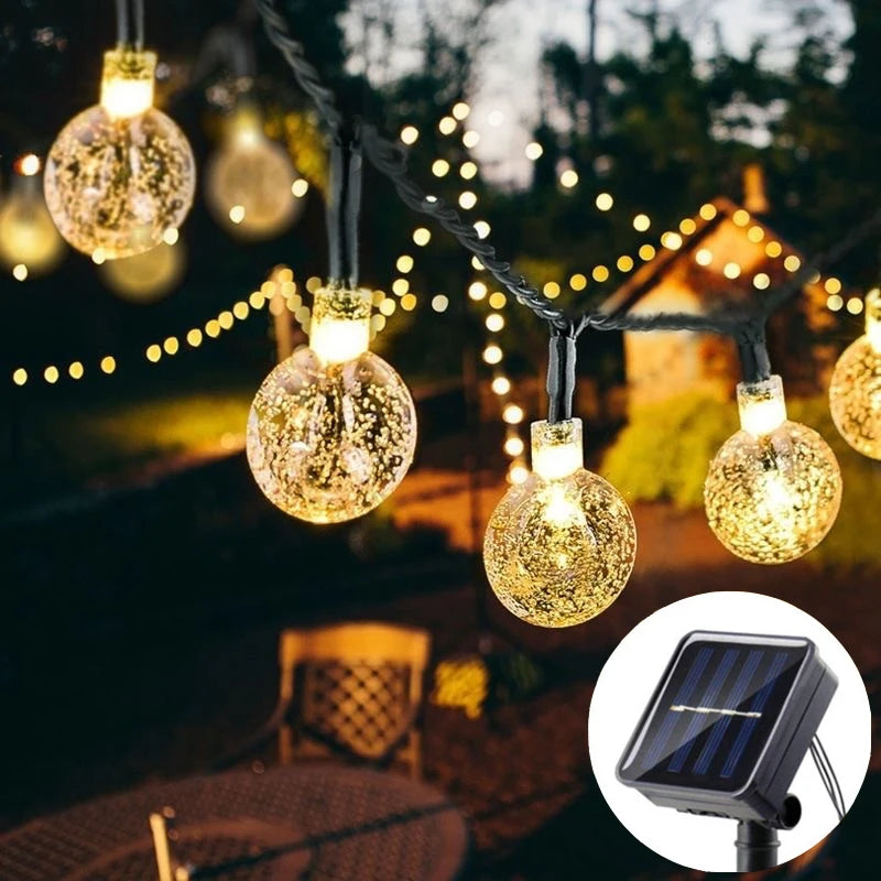 String lights with glass-like bulbs are strung outdoors in a dark setting, alongside a solar panel device.