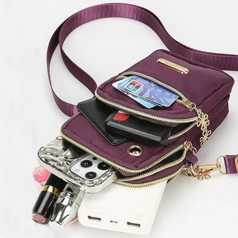 Bolso cruz de nylon morado lleno de accesorios electrónicos y una batería externa.