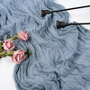 A light blue cotton gauze table runner draped with soft pink roses and black decorative tools.
