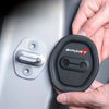 A hand holds a black silicone door lock protector with a silver latch, demonstrating the product.
