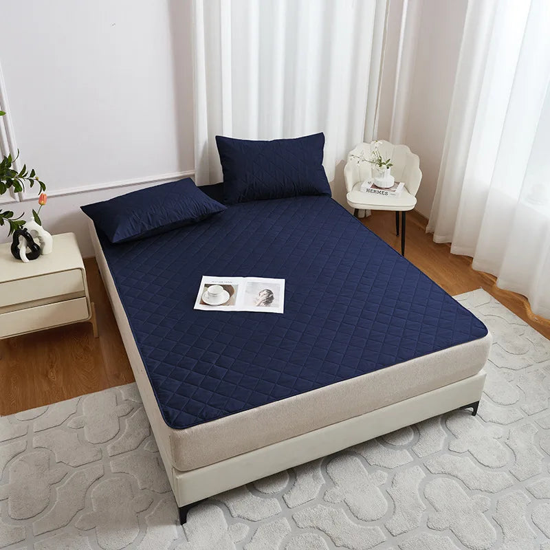 A navy blue waterproof mattress protector with elastic straps is displayed on a bed, next to a white chair and light-colored 