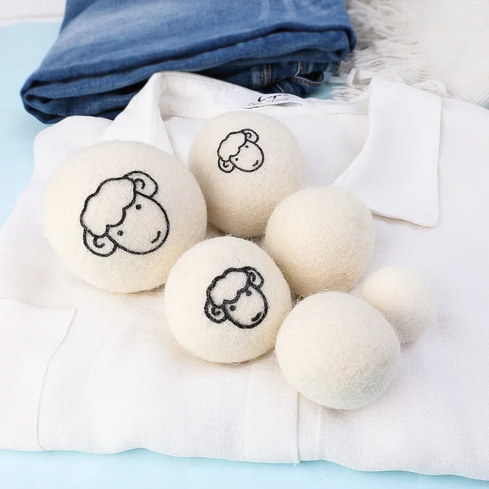 A set of six white wool dryer balls with embroidered sheep faces resting on a white fabric.