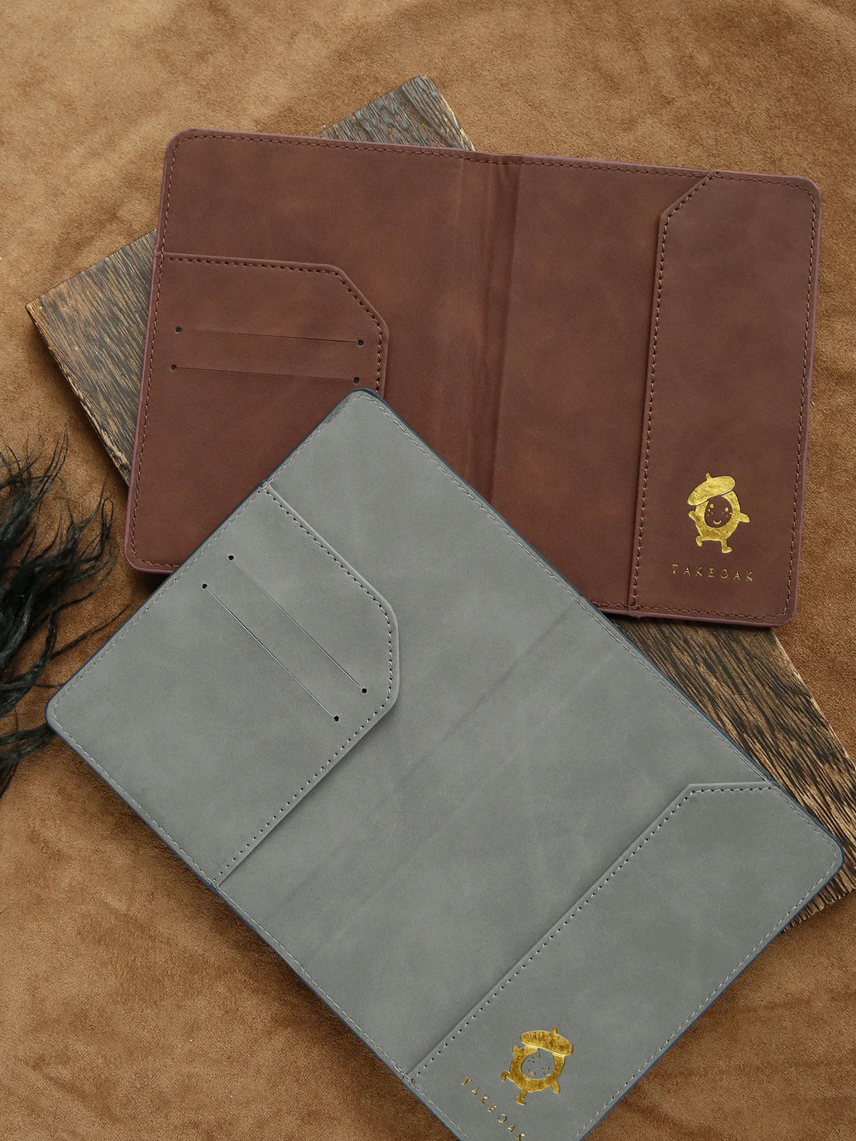 A brown leather passport holder and a gray leather cardholder are displayed on a tan fabric background.