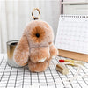 A fluffy orange bunny keychain with a pom pom tail hanging on a silver ring, placed on a checkered surface.