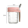 A clear glass jar with a pink lid and a wooden spoon, used for overnight oats or breakfast.