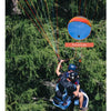 A person is preparing to launch a parachute with an orange and blue canopy in a dense green forest setting.