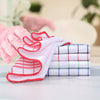 Pink gloved hand holding a stack of white and red checkered lint-free dish cloths on a white surface.