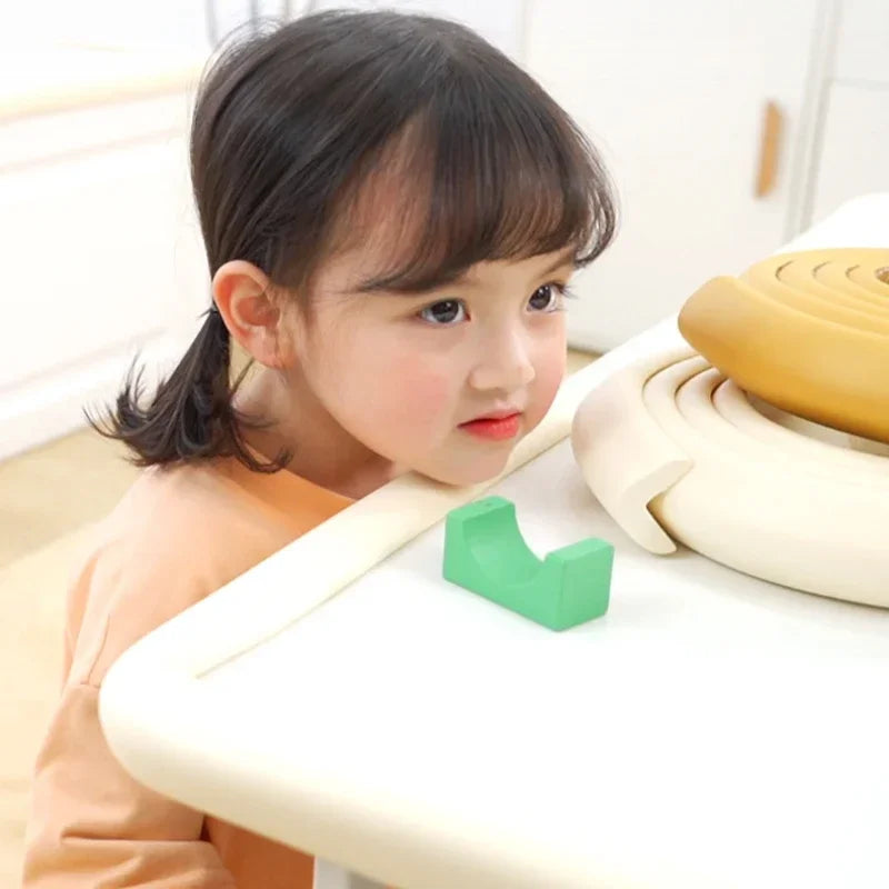 A young girl is interacting with a white table featuring soft green bumper strips designed to protect edges and corners.