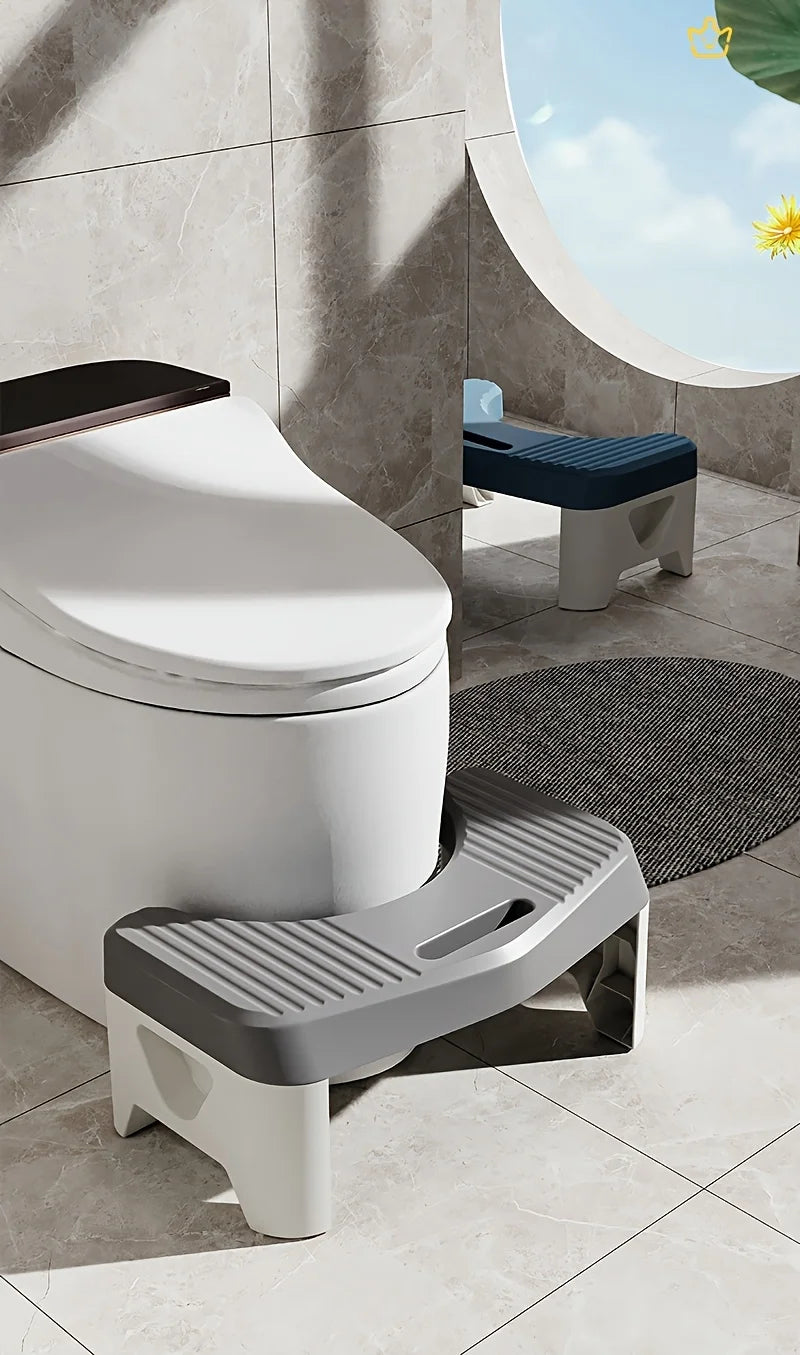 A white comfort squatting stool with a gray footrest is placed on a tiled floor next to a window.