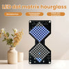 A black LED dot matrix hourglass display is shown on a white surface next to a potted plant.