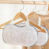 A white laundry bag designed for bras is hanging on a wooden hanger.