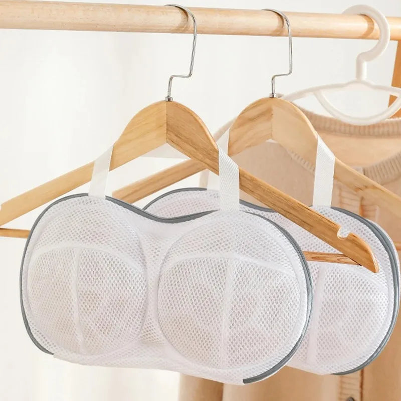 A white laundry bag designed for bras is hanging on a wooden hanger.