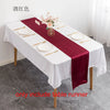 A white tablecloth set with a deep burgundy satin table runner, gold cutlery, and floral centerpiece.