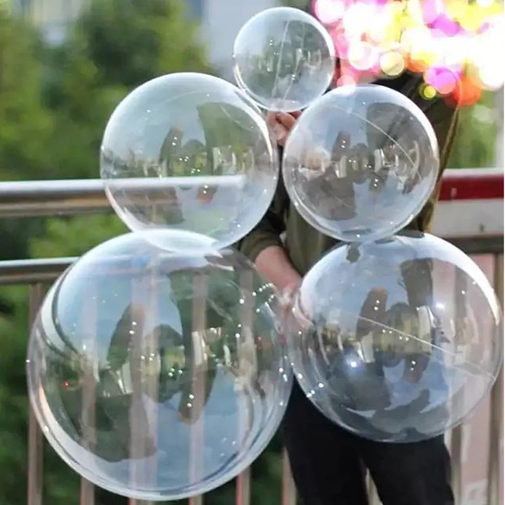 A person is holding a multi-pack of clear PVC balloons against a blurred outdoor background.
