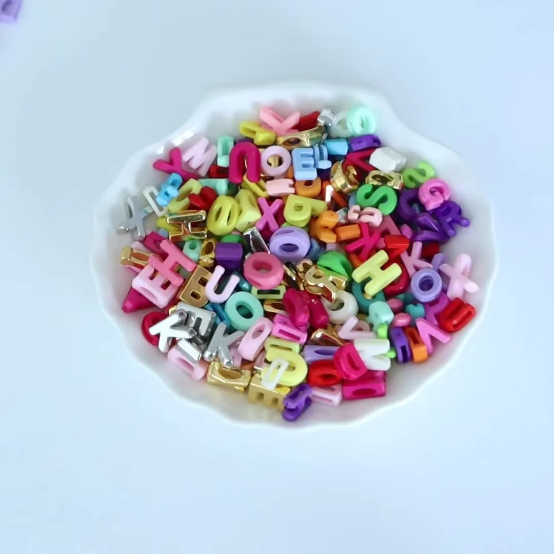 Haufen gemischter Buchstaben-Platzhalterperlen in verschiedenen Farben wie rosa, gelb, grün und lila auf einem weißen Teller