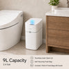 A white motion sensor trash can with a lid and a self-securing trash bag sitting on a wooden cabinet.