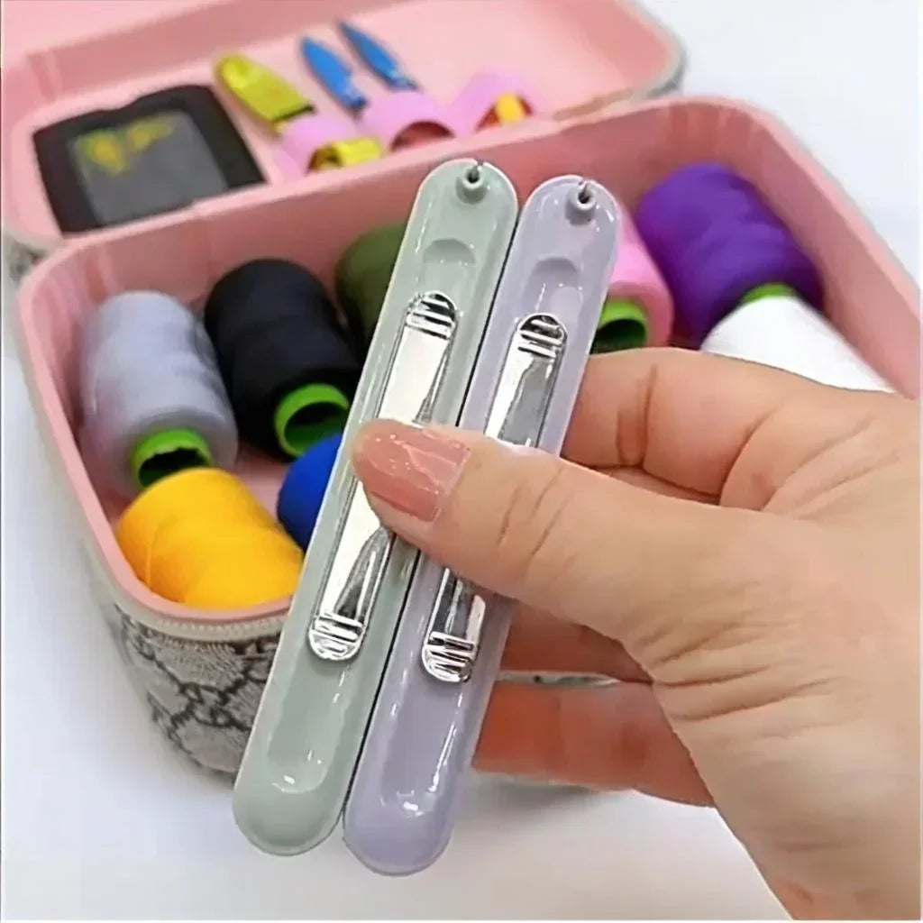 A hand holds a pair of purple and gray needle threader and seam ripper tools inside a pink storage box.