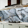 A kitchen backsplash featuring a gray marble pattern with gold veining and a stainless steel range hood.