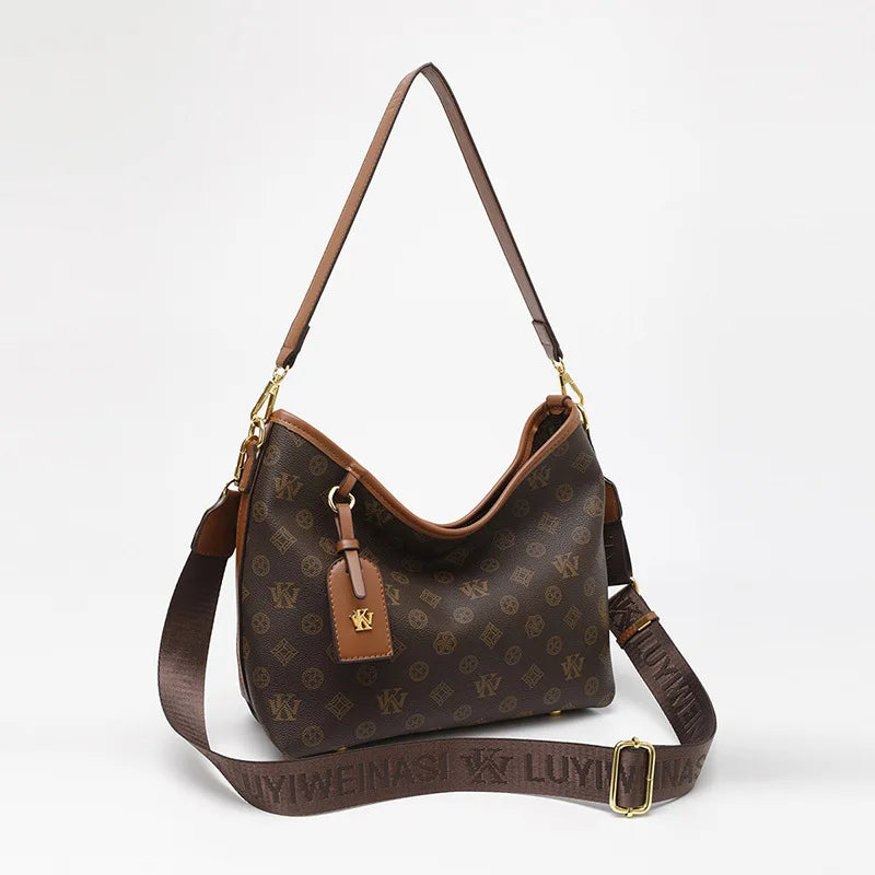A brown leather tote bag with a gold hardware detail and a detachable strap is shown against a white background.